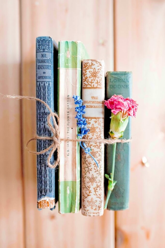 A pair of old-fashioned English literature books adorned with fresh flowers and tied with twine on a wooden shelf.