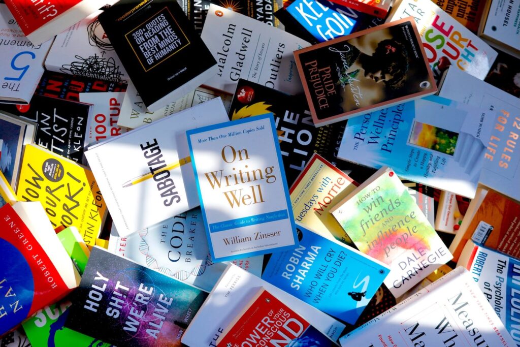 A scattered pile of popular English paperbacks including books on writing well and personal development.