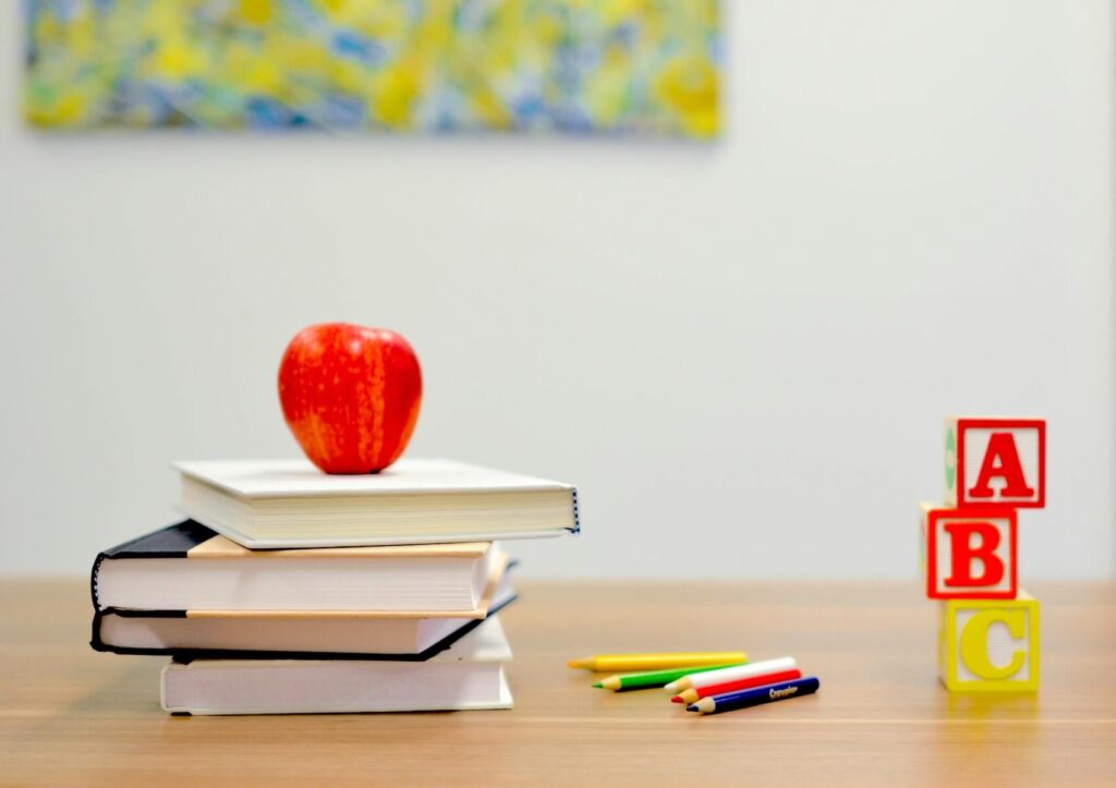 A red apple resting on a stack of English textbooks next to colorful crayons and ABC wooden blocks.