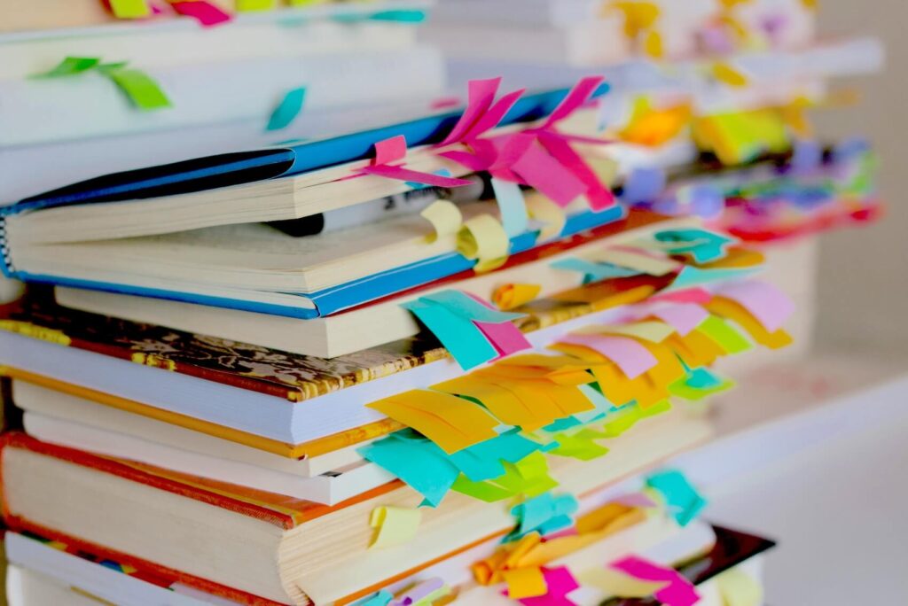 A tall stack of English study textbooks heavily marked with vibrant colorful sticky notes for exam preparation.