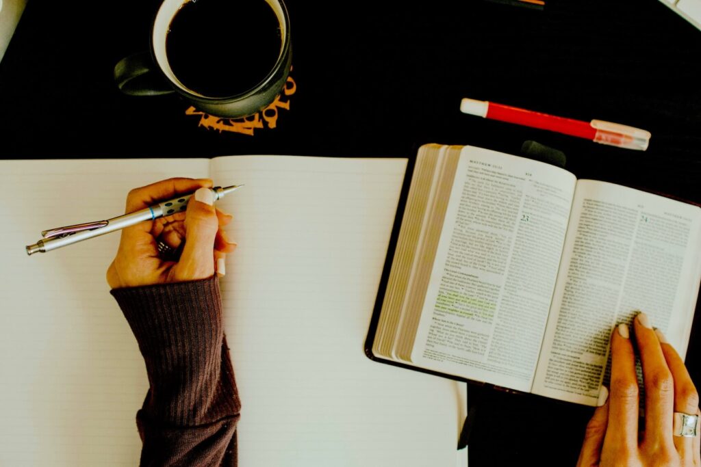 Top-down view of a person hand-writing notes in an open English dictionary next to a cup of coffee.