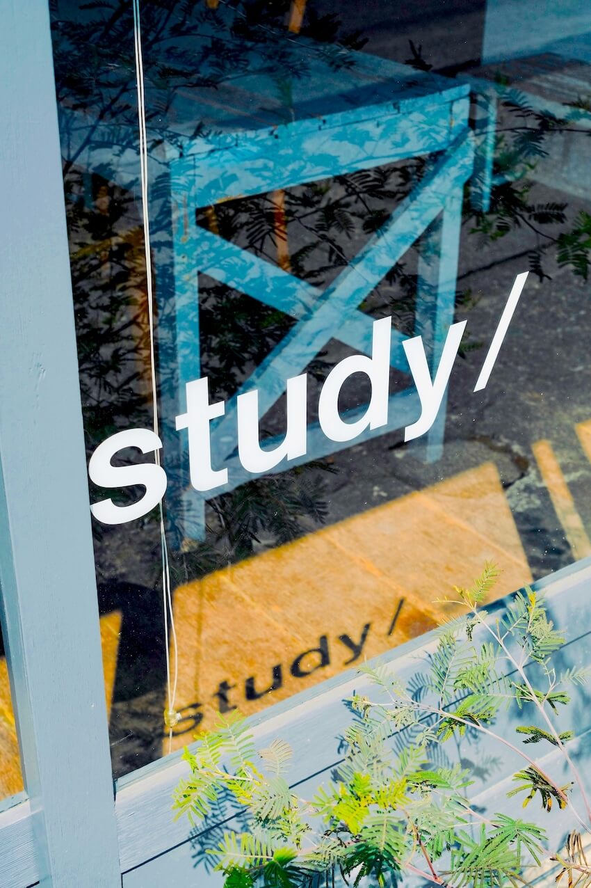 A modern glass door with the word study printed repeatedly situated near a blue bench and potted plants for an English learning environment.