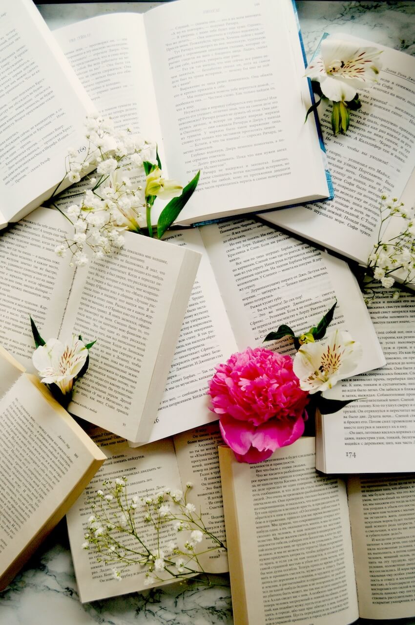Several open English learning textbooks overlapping each other decorated with white and pink spring flowers.
