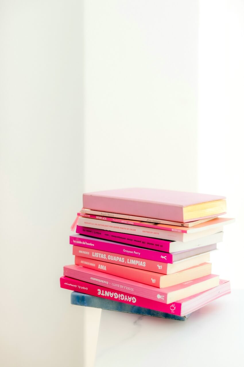 A neatly stacked pile of pink and red English reading books resting on a clean white surface.